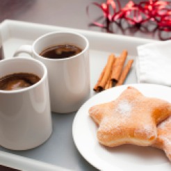 Christmas coffee break with two cups of espresso and two festive star-shaped sugared doughnuts laid out on a tray